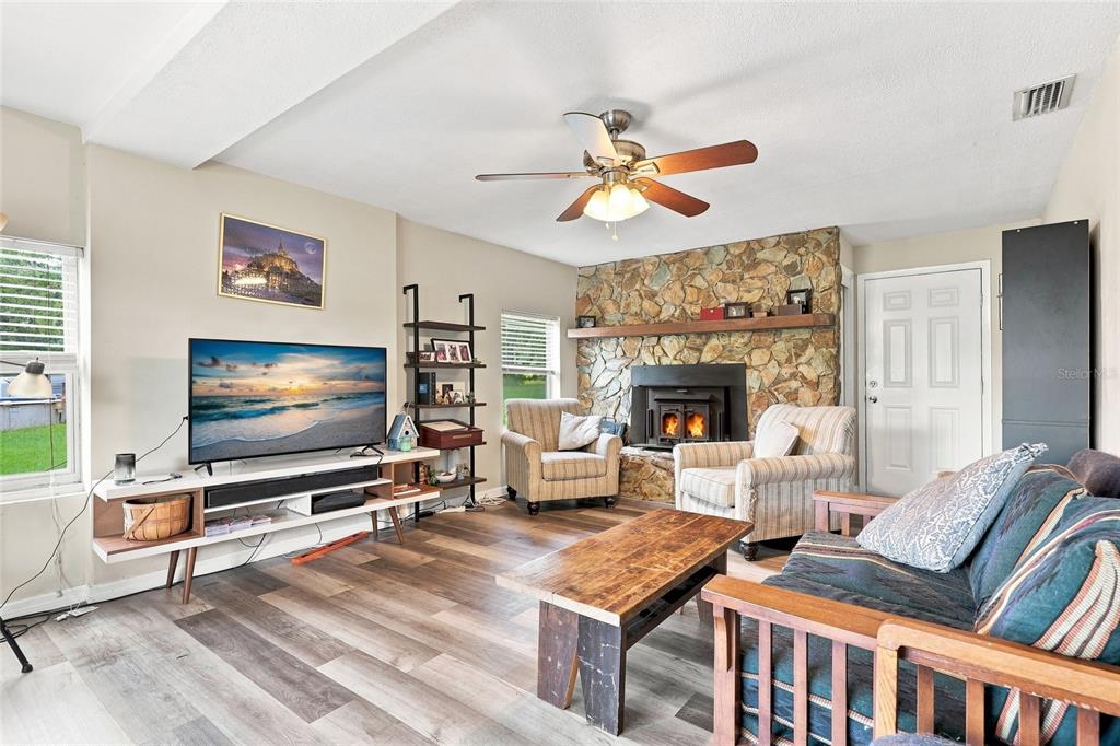 A living room features wood-look flooring, a stone fireplace, a ceiling fan, and a television — 16488 SW 139TH AVENUE, ARCHER, FL