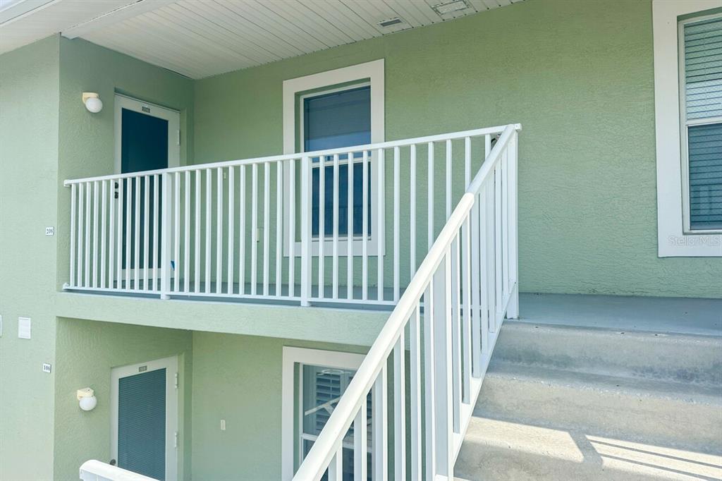 An exterior view shows a two-story building with green stucco walls and white metal railings — 8100 MEMORY LANE UNIT 208, ROTONDA WEST, FL