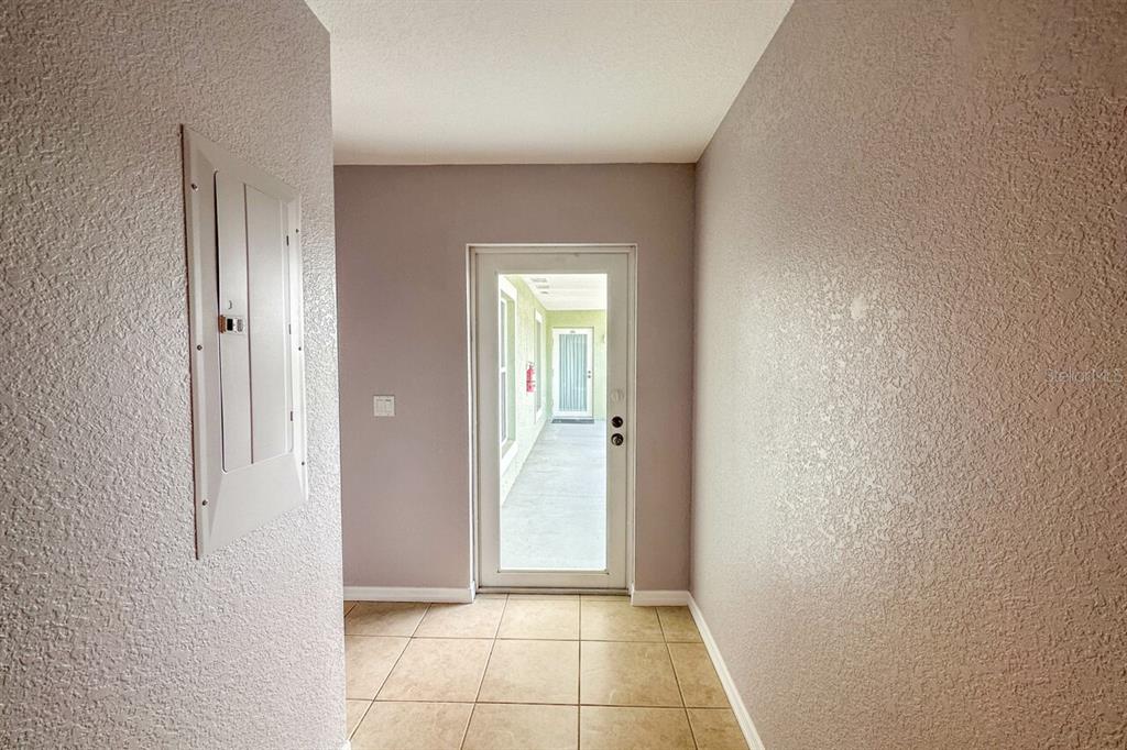 A hallway with tiled flooring leads to a glass door opening onto a covered patio — 8100 MEMORY LANE UNIT 208, ROTONDA WEST, FL
