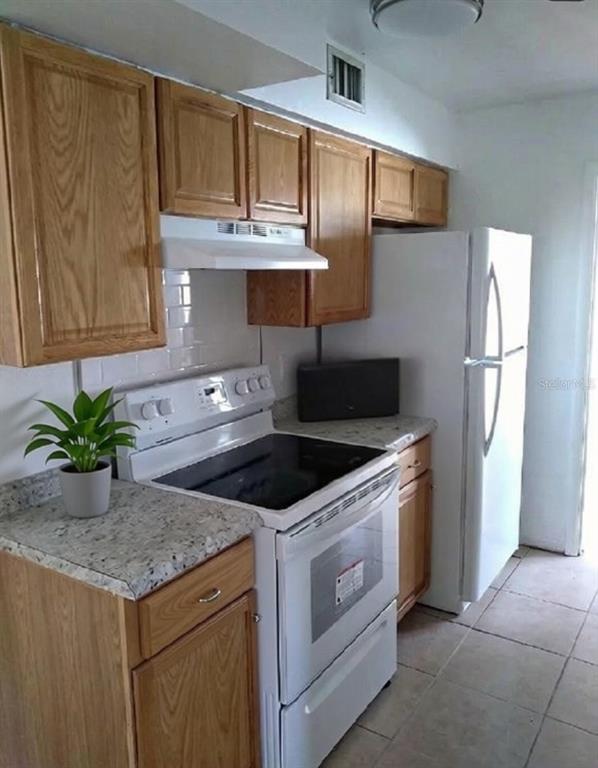 A kitchen features wood cabinets, white appliances, a tiled backsplash, and speckled laminate countertops — 1001 BAY BREEZE TERRACE, LARGO, FL