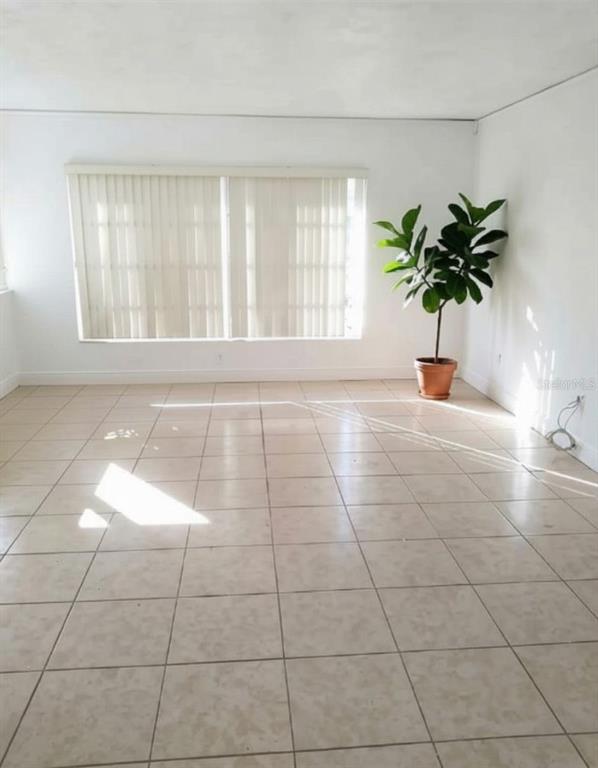 An empty room features white walls, light-colored tile flooring, vertical blinds, and a potted plant — 1001 BAY BREEZE TERRACE, LARGO, FL