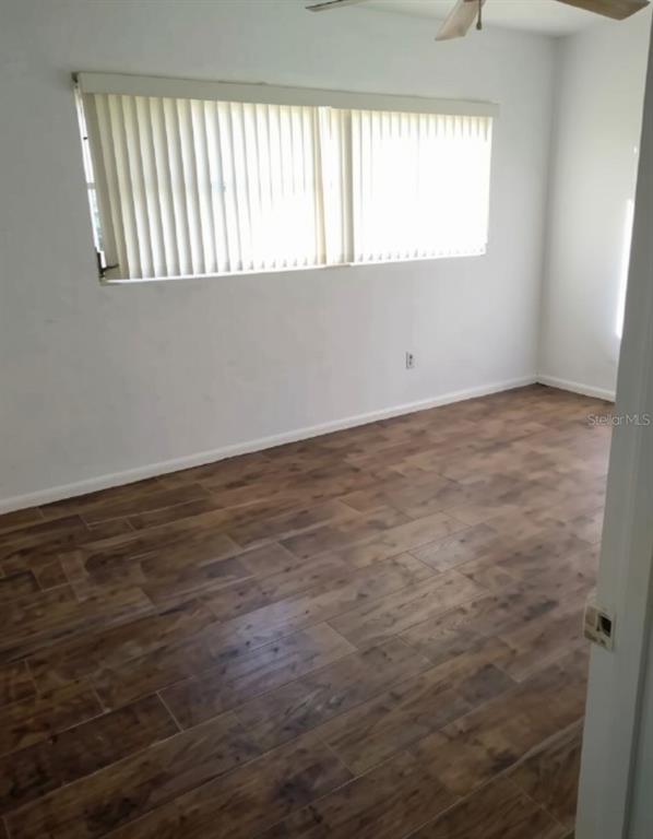 An empty room features wood-look tile flooring, white walls, and a large window with blinds — 1001 BAY BREEZE TERRACE, LARGO, FL