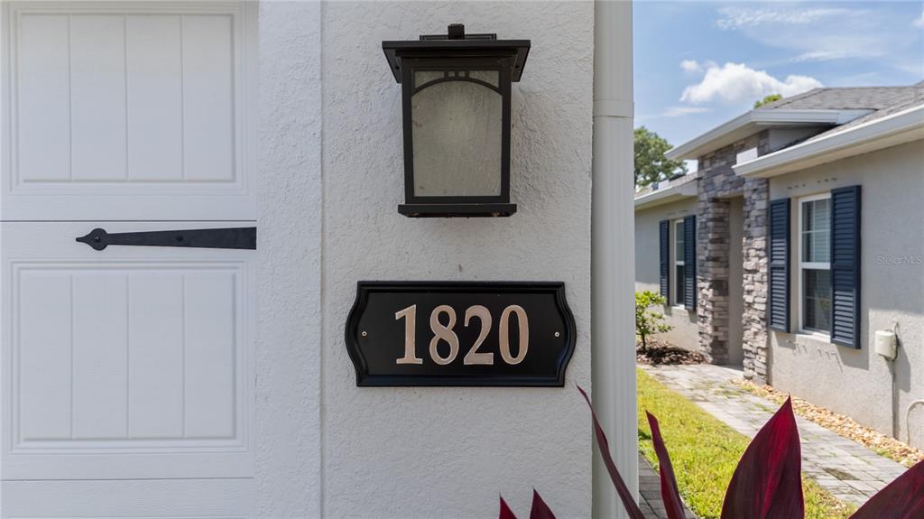 A house number plaque reading 1820 is mounted on a white exterior wall below a lantern — 1820 W PALMS DRIVE, PORT CHARLOTTE, FL