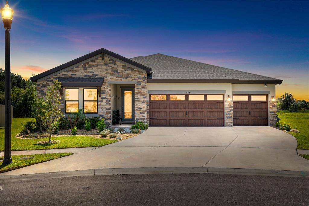 A single-story house with a stone facade, a three-car garage, and a concrete driveway — 13098 WELLSPRING DRIVE, LITHIA, FL