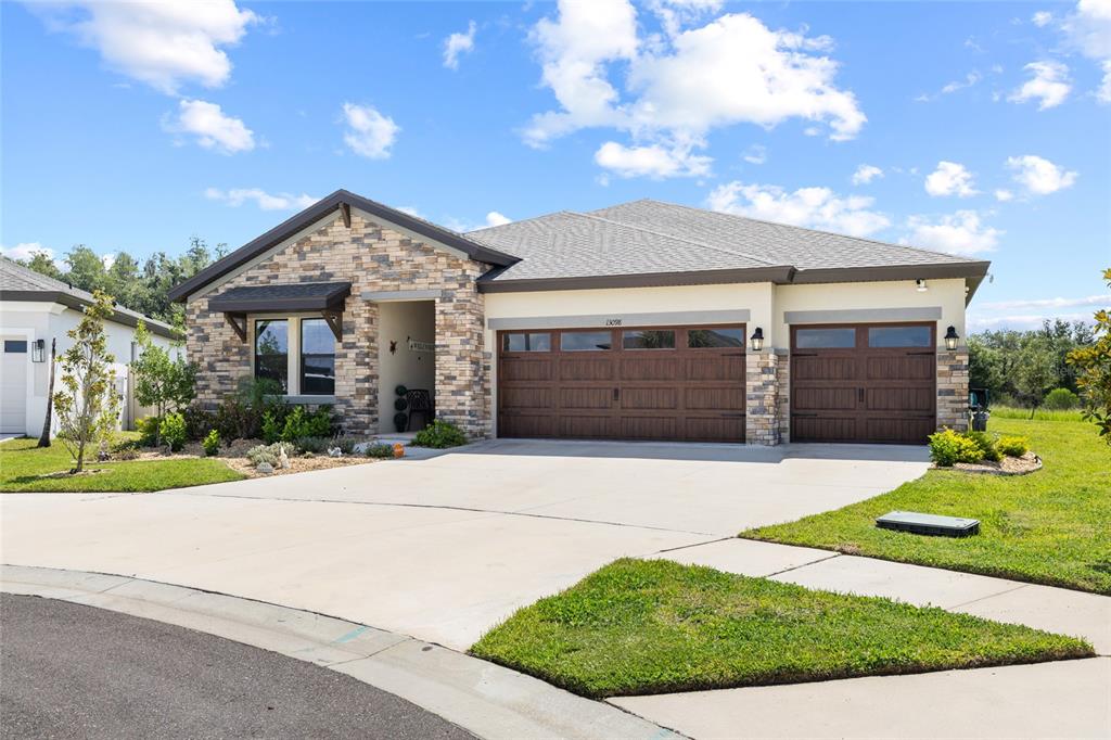 A single-story house with a stone facade, a three-car garage, and a concrete driveway — 13098 WELLSPRING DRIVE, LITHIA, FL