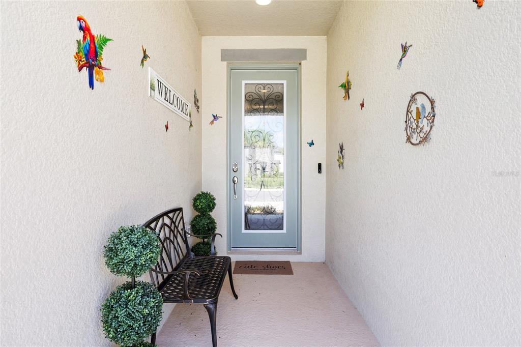 A covered entryway features a light blue glass-paneled door, a metal bench, and wall decorations — 13098 WELLSPRING DRIVE, LITHIA, FL