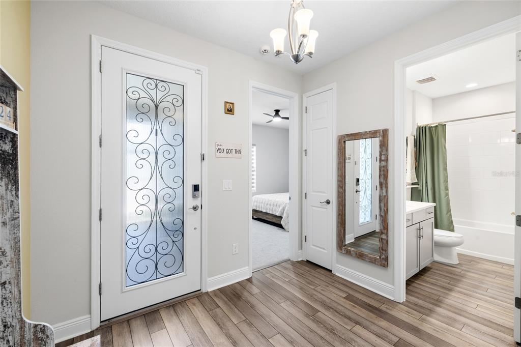 An entryway with wood-look flooring, a glass-paneled front door, a bedroom doorway, and a bathroom — 13098 WELLSPRING DRIVE, LITHIA, FL
