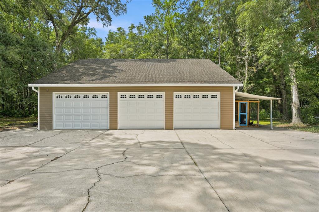 A detached three-car garage with tan siding and a concrete driveway sits among trees — 18308 VALOR PATH, BROOKSVILLE, FL