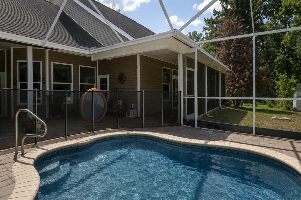 A swimming pool sits on a paved patio enclosed by a screened lanai and fence — 18308 VALOR PATH, BROOKSVILLE, FL