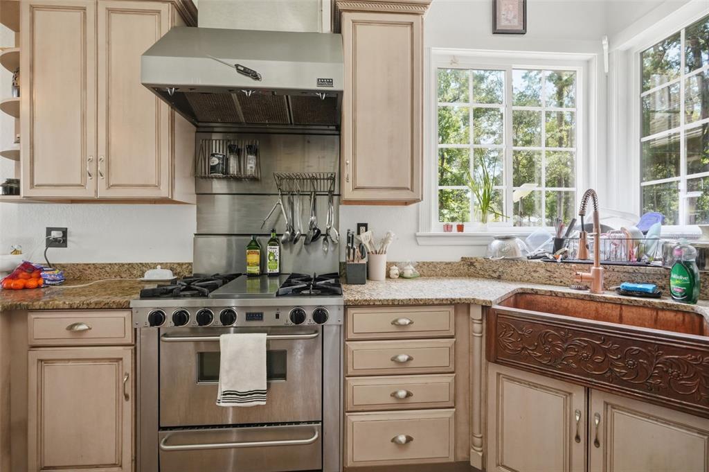 A kitchen features light wood cabinets, a stainless steel range, and a decorative copper farmhouse sink — 18308 VALOR PATH, BROOKSVILLE, FL