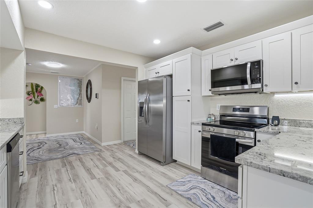 A kitchen features white cabinets, stainless steel appliances, granite countertops, and light wood-look flooring — 3332 GULF WINDS CIRCLE, HERNANDO BEACH, FL