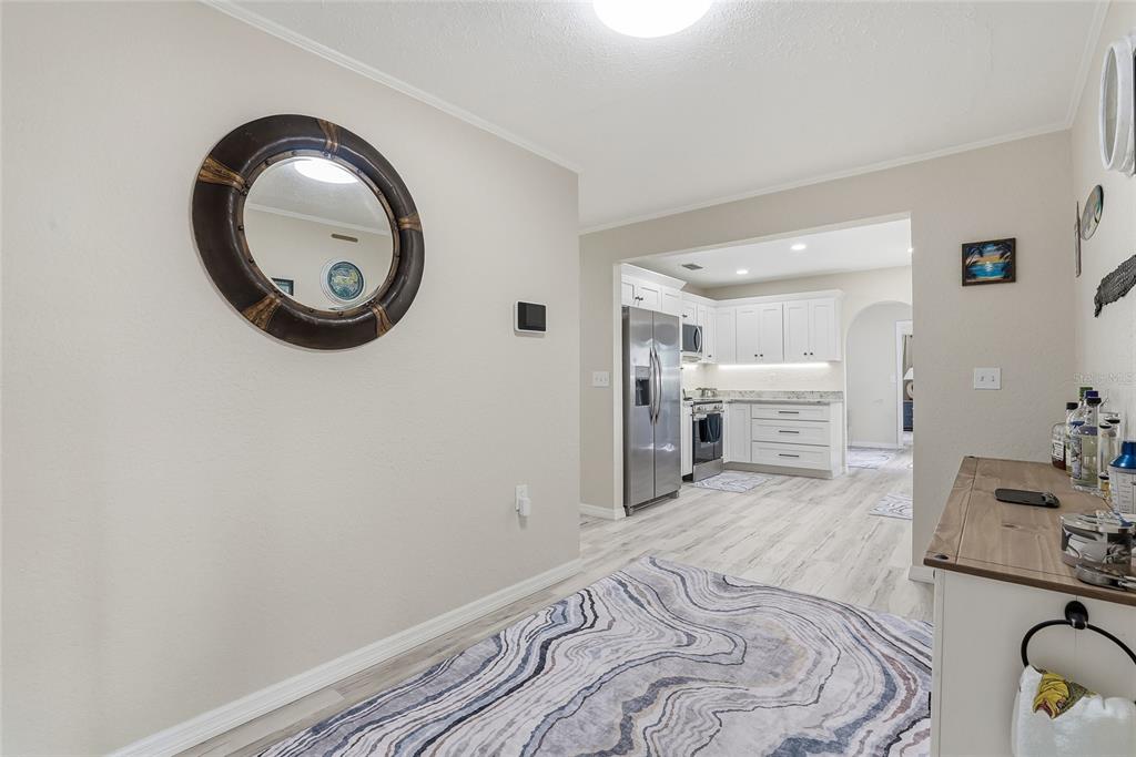 A dining area with a round mirror leads into a kitchen featuring white cabinets — 3332 GULF WINDS CIRCLE, HERNANDO BEACH, FL