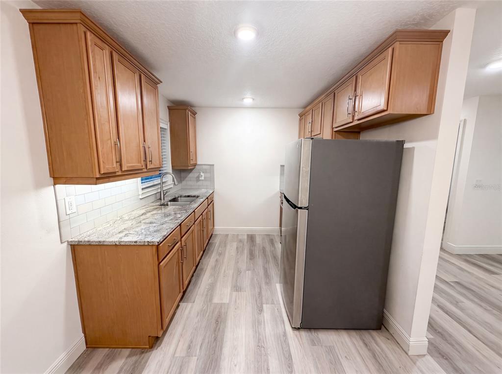 A kitchen features wood cabinets, granite countertops, a stainless steel refrigerator, and light wood flooring — 3444 VALEVIEW DRIVE, APOPKA, FL