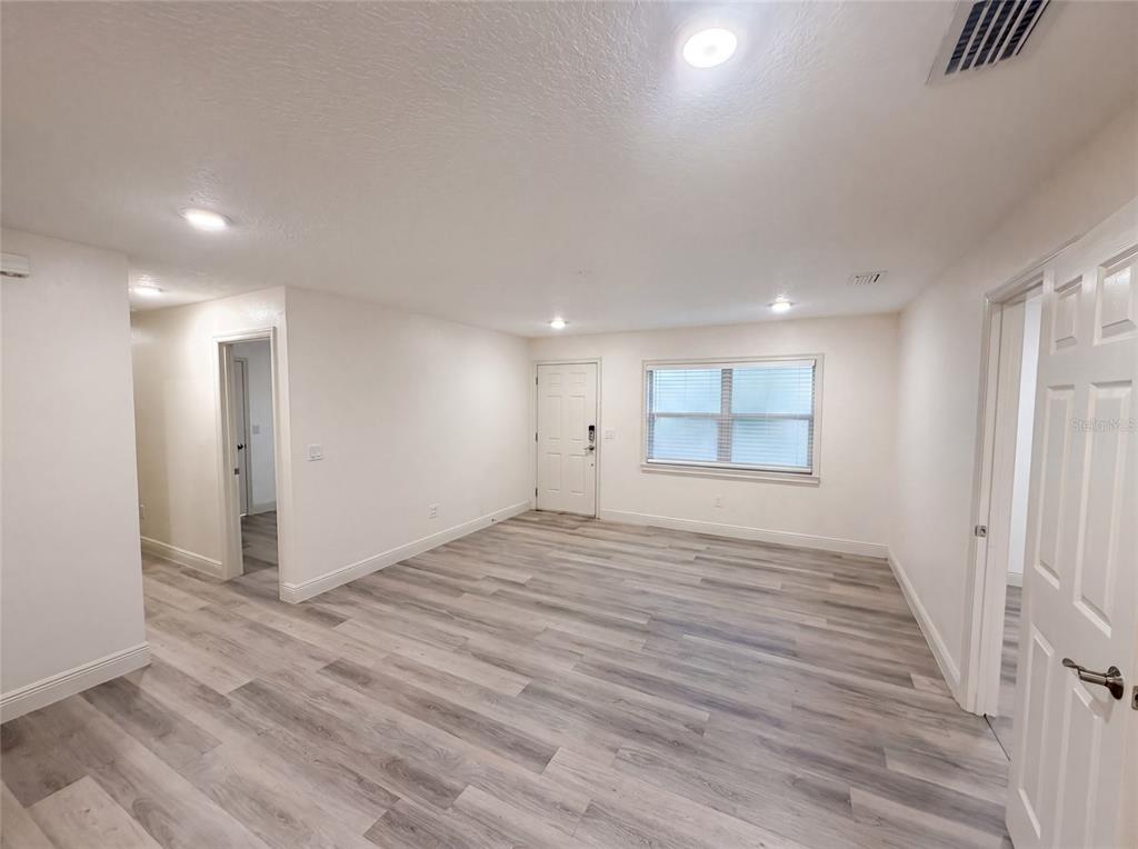An empty room with light wood-look flooring, white walls, a front door, and a window — 3444 VALEVIEW DRIVE, APOPKA, FL