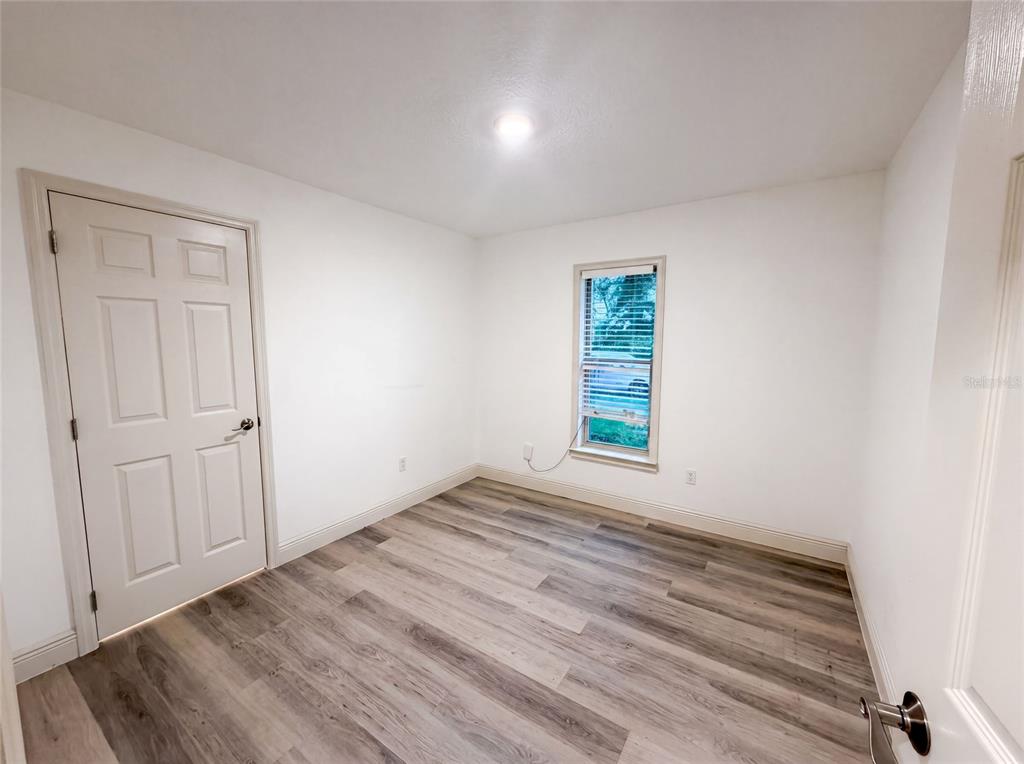 An empty room with white walls, light wood-look flooring, a window, and a closed door — 3444 VALEVIEW DRIVE, APOPKA, FL
