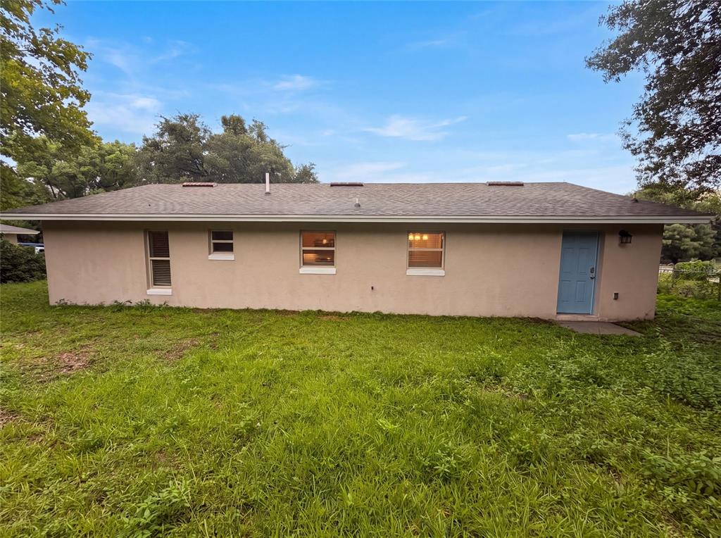 The exterior rear view of a single-story house with a blue door and lawn — 3444 VALEVIEW DRIVE, APOPKA, FL