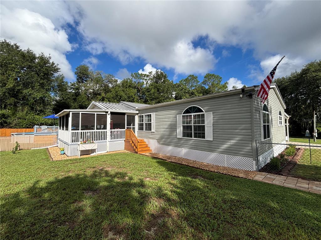 A gray manufactured home features a screened-in porch, white lattice skirting, and an American flag — 1762 SE 173RD AVENUE, SILVER SPRINGS, FL