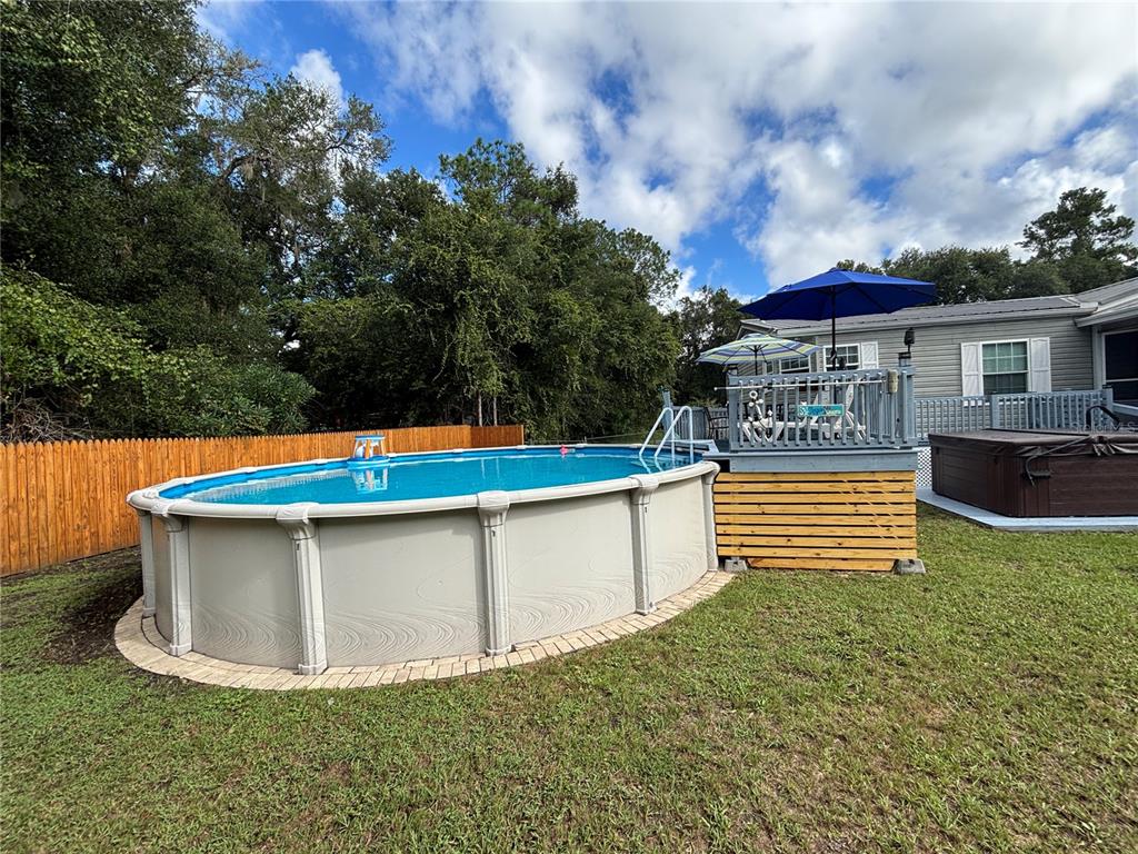 An oval above-ground swimming pool sits next to a wooden deck with a blue umbrella — 1762 SE 173RD AVENUE, SILVER SPRINGS, FL