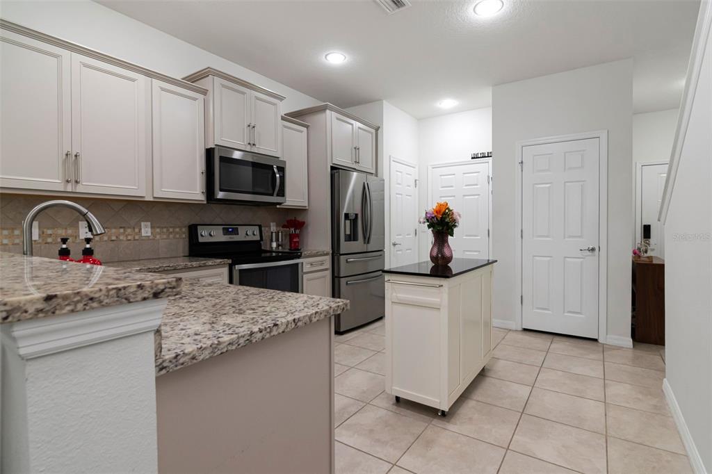 A kitchen features light-colored cabinetry, granite countertops, stainless steel appliances, and a mobile island — 9213 HILLCROFT DRIVE, RIVERVIEW, FL