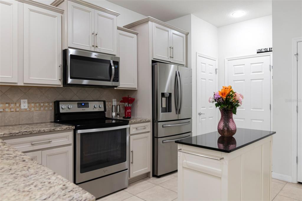 A kitchen features stainless steel appliances, light-colored cabinetry, granite countertops, and a small center island — 9213 HILLCROFT DRIVE, RIVERVIEW, FL