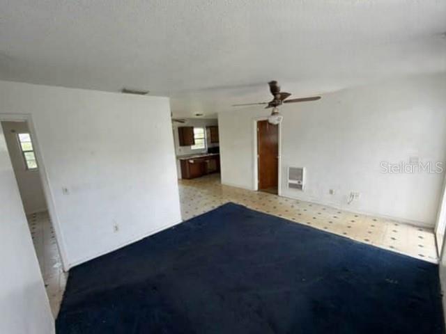 A living room with dark blue carpeting, a ceiling fan, and an adjacent kitchen area — 904 SE HALL STREET, STUART, FL