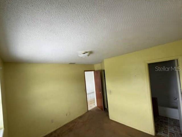 An empty bedroom with yellow walls, brown carpet, and a doorway leading to a bathroom — 904 SE HALL STREET, STUART, FL