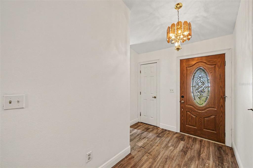 An entryway features wood-look flooring, a white door, a decorative wood front door, and chandelier — 748 PINE SHORES CIRCLE, NEW SMYRNA BEACH, FL