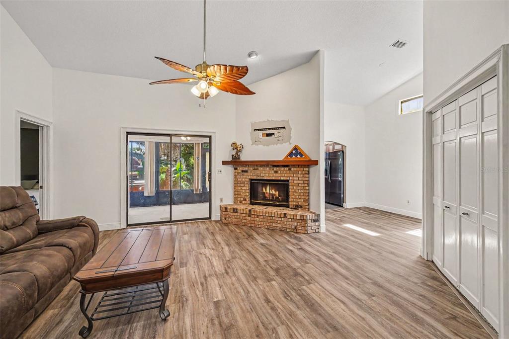 A living room features a brick fireplace, wood-look flooring, a ceiling fan, and sliding glass doors — 748 PINE SHORES CIRCLE, NEW SMYRNA BEACH, FL
