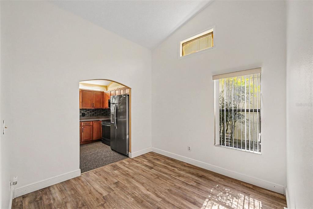 A room with wood-look flooring, vaulted ceilings, a window, and an arched doorway to a kitchen — 748 PINE SHORES CIRCLE, NEW SMYRNA BEACH, FL
