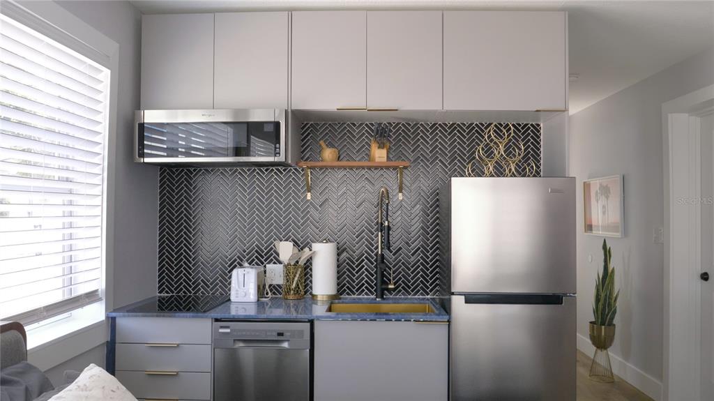 A small kitchen features gray cabinetry, stainless steel appliances, and a black herringbone tile backsplash — 137 N HOLLYWOOD AVENUE, DAYTONA BEACH, FL