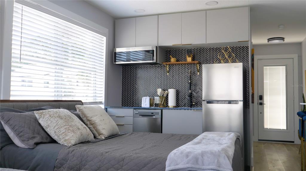 A studio apartment features a bed next to a kitchenette with gray cabinets and backsplash — 137 N HOLLYWOOD AVENUE, DAYTONA BEACH, FL