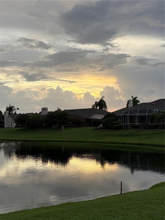 A pond in the foreground reflects a sunset sky behind several suburban houses — 5092 KILTY COURT E, BRADENTON, FL