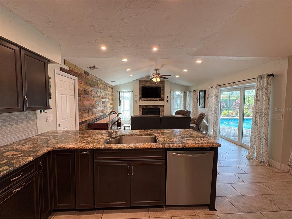 A kitchen with granite countertops and dark cabinets overlooks a living room with a fireplace — 5092 KILTY COURT E, BRADENTON, FL