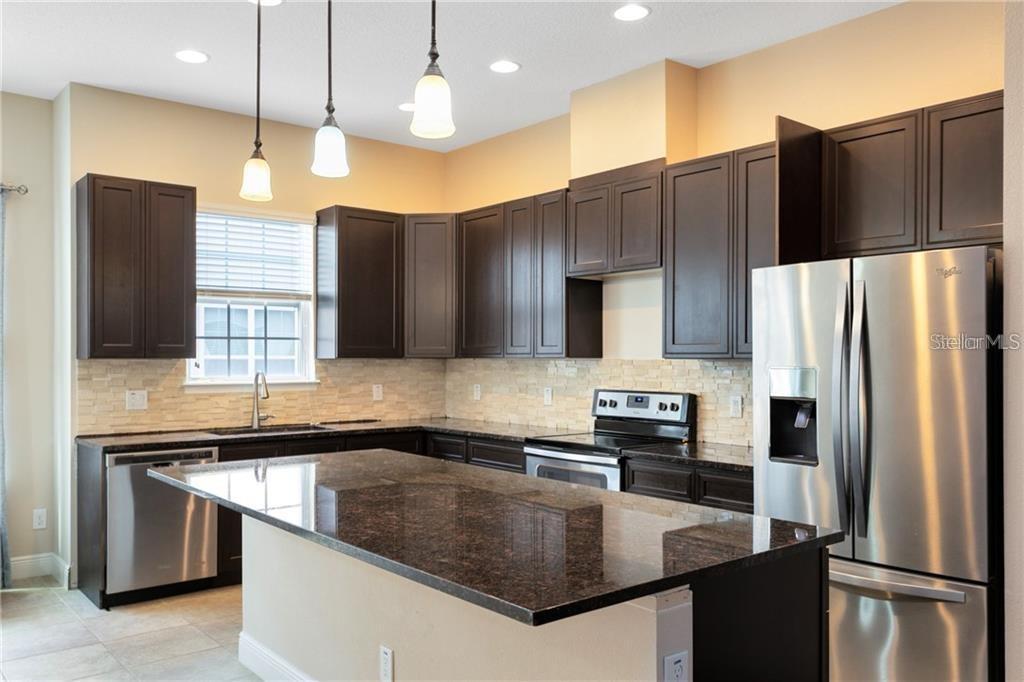 A kitchen features dark wood cabinets, granite countertops, stainless steel appliances, and a central island — 1412 LOBELIA DRIVE, LAKE MARY, FL