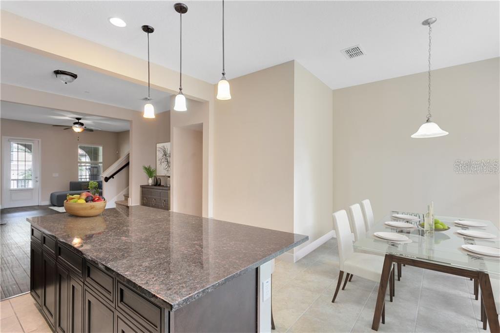 A kitchen island with dark cabinets and granite countertops sits beside a glass dining table — 1412 LOBELIA DRIVE, LAKE MARY, FL