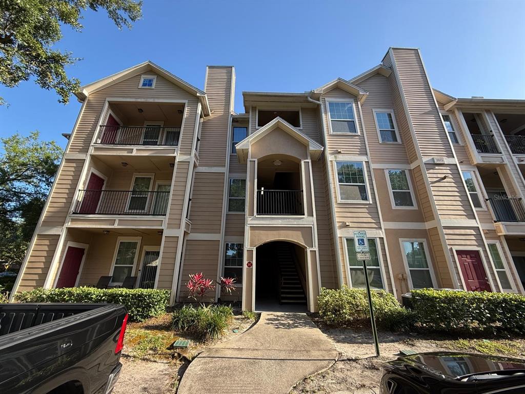 A multi-story apartment building exterior features tan siding, a central stairwell, and a handicap parking sign — 2015 ERVING CIRCLE UNIT 307, OCOEE, FL