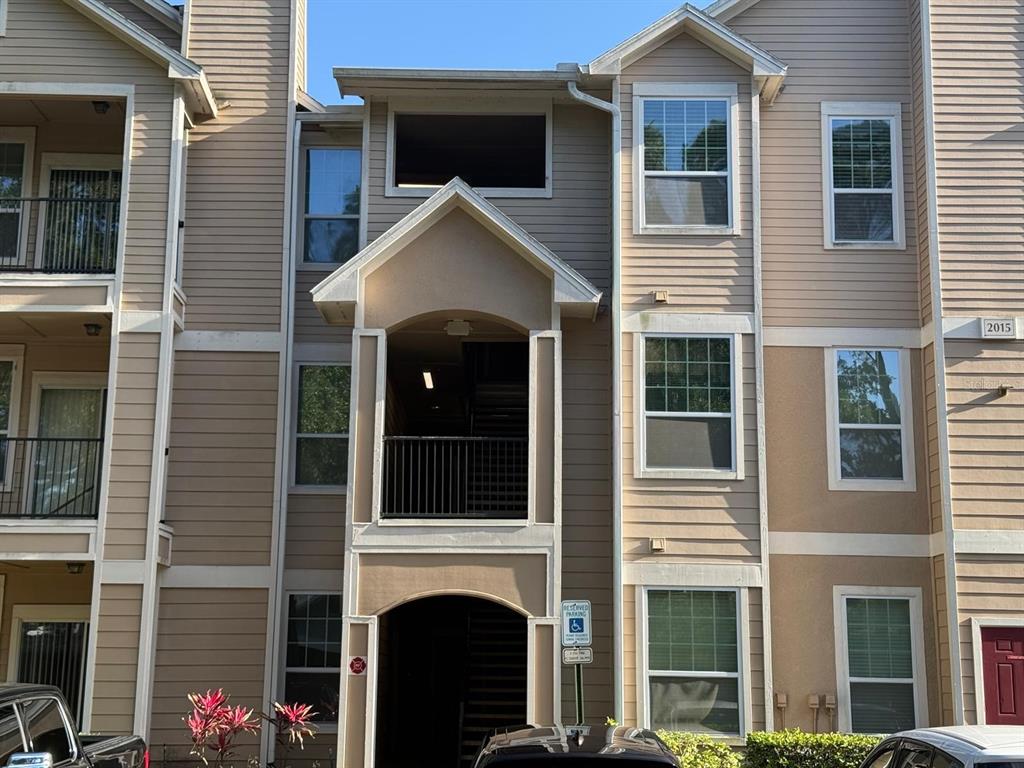A three-story apartment building exterior with tan siding, balconies, and a central stairwell entrance — 2015 ERVING CIRCLE UNIT 307, OCOEE, FL