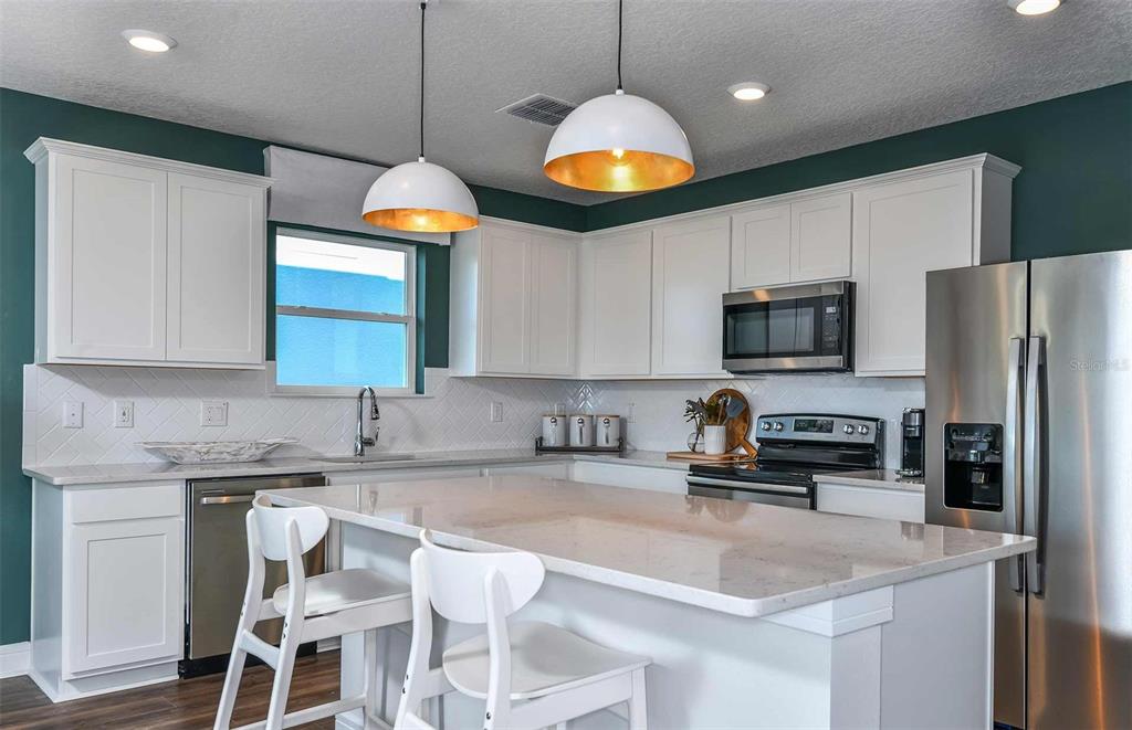 A kitchen features white cabinets, a quartz island, stainless steel appliances, and dark green walls — 10511 SAPPHIRE BREEZE COVE, PARRISH, FL