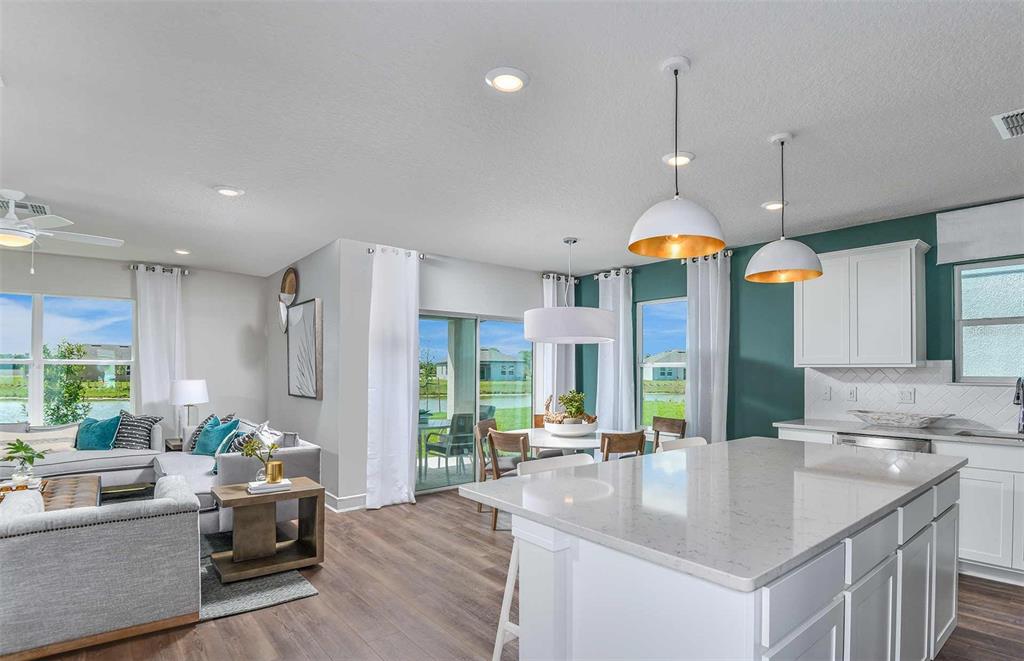 An open-concept kitchen and living area featuring a large island, white cabinets, and sliding doors — 10511 SAPPHIRE BREEZE COVE, PARRISH, FL