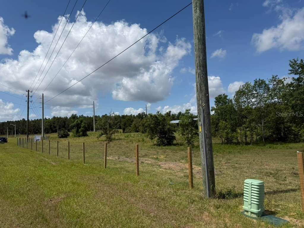 A grassy, fenced-in vacant lot features a utility pole and power lines under a blue sky — 22029 COUNTY ROAD 561, ASTATULA, FL