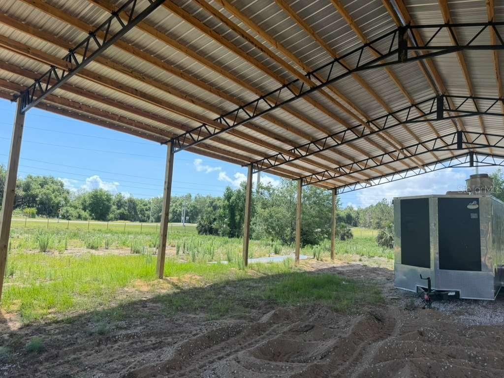 An open-sided metal pole barn structure stands over a dirt ground with a trailer parked inside — 22029 COUNTY ROAD 561, ASTATULA, FL