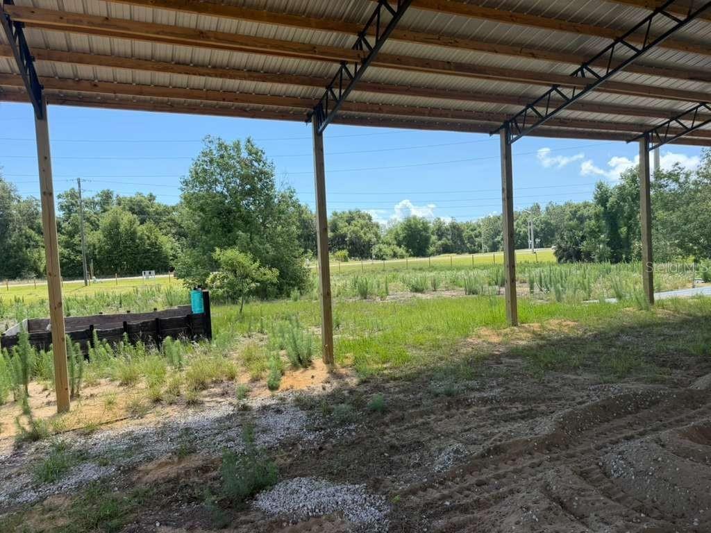 A view from under a metal-roofed pole barn looking out over a grassy, undeveloped lot — 22029 COUNTY ROAD 561, ASTATULA, FL
