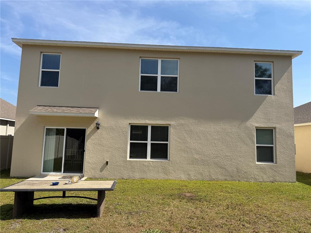 The rear exterior of a two-story beige house features a sliding glass door and windows — 328 CONWAY AVENUE, ST CLOUD, FL