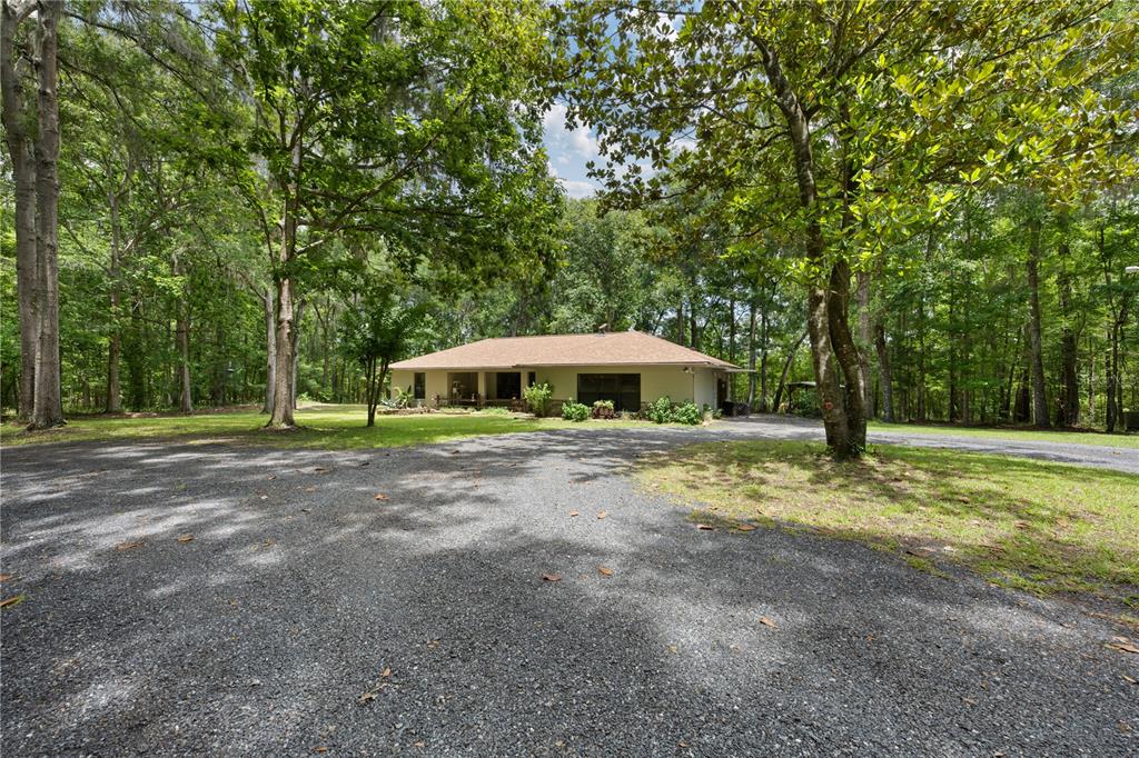 A single-story house with a gravel driveway sits in a wooded lot — 18451 NW 141ST AVENUE, WILLISTON, FL