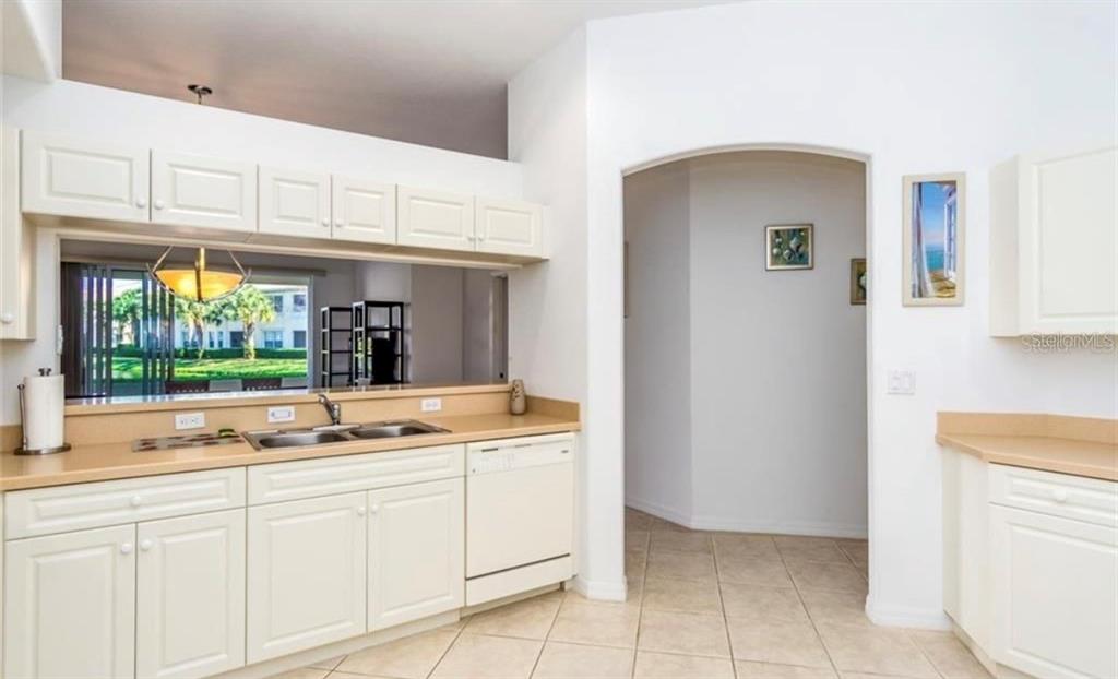 A kitchen with white cabinets, tan countertops, and a pass-through window overlooking an outdoor area — 1604 TRIANO CIRCLE UNIT 1604, VENICE, FL