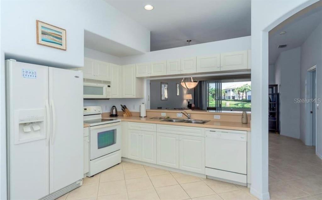 A kitchen with white cabinets, white appliances, and a pass-through window overlooking the living area — 1604 TRIANO CIRCLE UNIT 1604, VENICE, FL