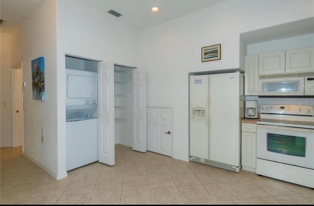 A kitchen area features white appliances, tile flooring, a laundry closet, and a pantry door — 1604 TRIANO CIRCLE UNIT 1604, VENICE, FL