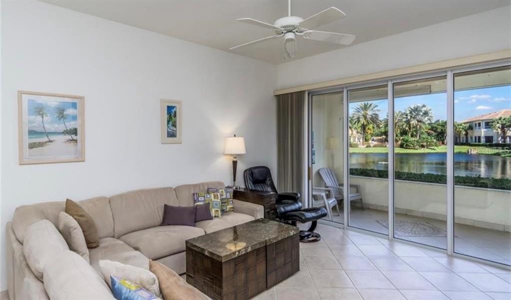 A living room with a beige sectional, a stone coffee table, and sliding glass doors outdoors — 1604 TRIANO CIRCLE UNIT 1604, VENICE, FL