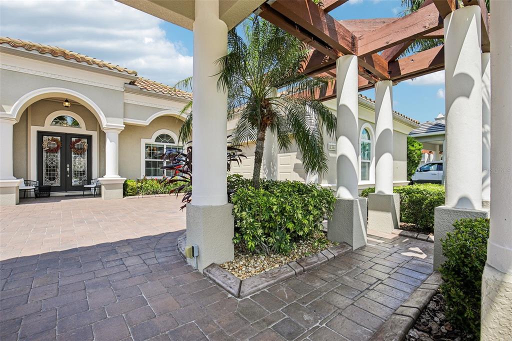 A paved courtyard features a wooden pergola, white columns, a palm tree, and double doors — 4741 MAINSAIL DRIVE, BRADENTON, FL