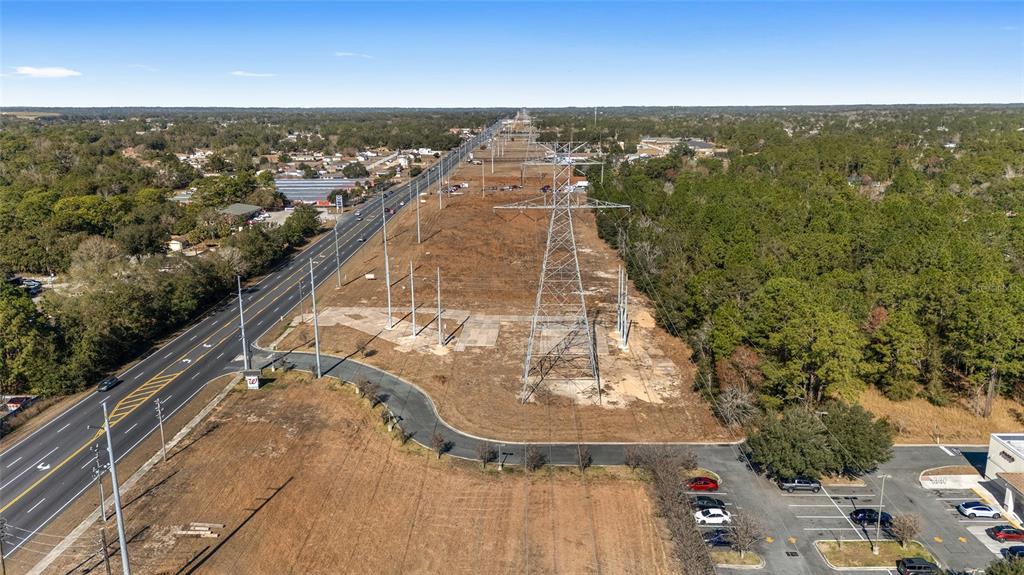 An aerial view shows a multi-lane road running alongside a large utility easement with towers — MARICAMP ROAD, OCALA, FL